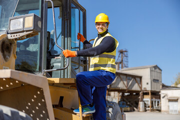 Smiling man factory engineer looking at camera and smiling while standing on steps of industrial truck