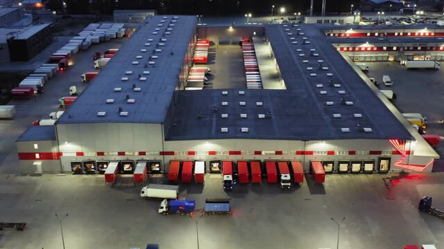 Aerial view of a logistics park with warehouse. A lot of semi-trucks and cargo trailers standing at ramps for loading and unloading goods at night