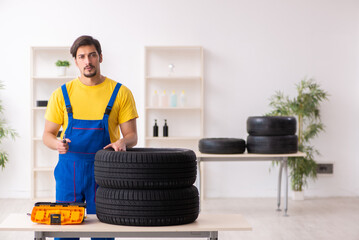 Fototapeta na wymiar Young male garage worker with tyre at workshop