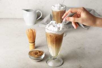 Female hand with glasses of iced hojicha latte on light background