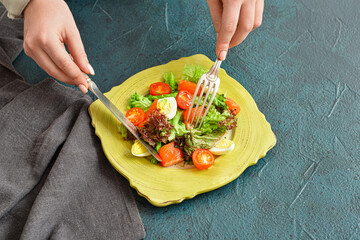 Woman eating tasty salad with salmon and vegetables at table