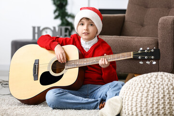 Little boy in Santa hat playing guitar at home