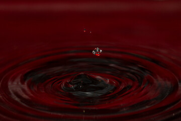 Unusual shaped water orb above red water ripples - stock photo