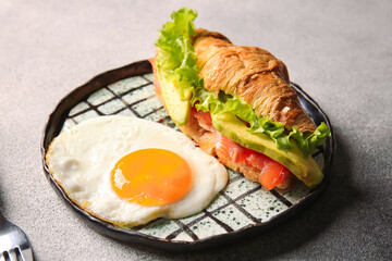 Plate of delicious croissant sandwich with egg on light background