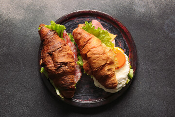 Plate with delicious croissant sandwiches on black background