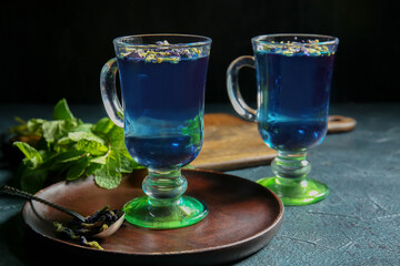 Glass cups of organic blue tea, dried flowers and mint on dark background