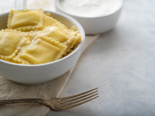 Ravioli drizzled with melted butter, fork and sour cream sauce on a white plate. Pastel shades. Close-up. Advertising, menu design, culinary blog, restaurant, cafe, hotel, home cooking.
