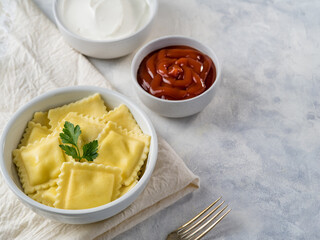 A portion of Italian ravioli with a parsley leaf on top and two sauces - tomato and sour cream on a white plate. Italian food. Restaurant, hotel, cafe, home cooking, cookbook.