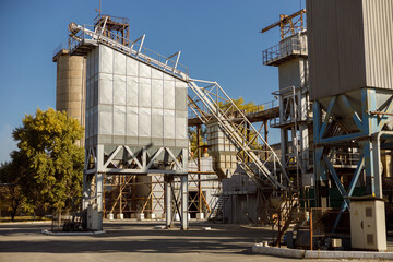 Factory or production plant with buildings, ladders and trees against blue sky