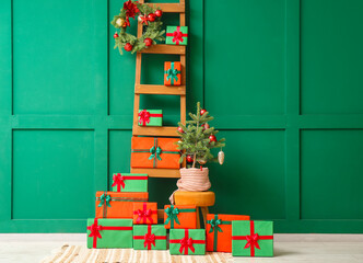 Wooden ladder with small Christmas tree and gifts near green wall