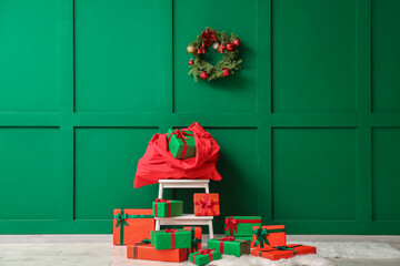 Stepladder with Santa bag and gifts near green wall