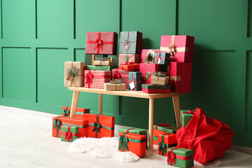 Wooden bench with Christmas gifts and Santa bag near green wall