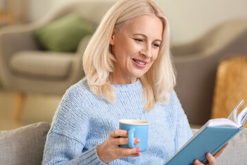 Beautiful mature woman reading book and drinking tea at home