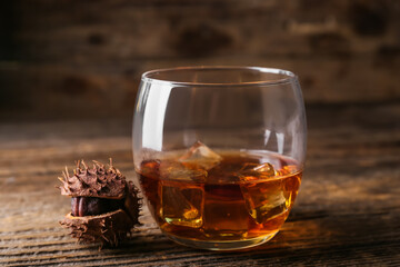 Glass of chestnut whiskey on wooden background