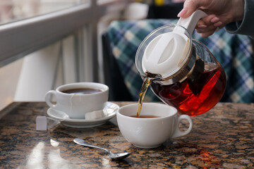Woman pouring hot tea into cup at table in cafe