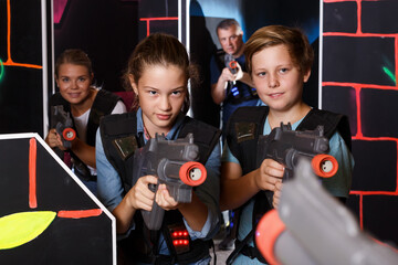 Excited teenagers holding laser guns at other players during laser tag game with parents indoors..