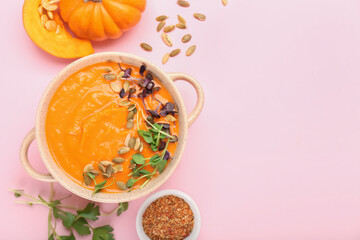 Pot with tasty pumpkin cream soup, spices and seeds on color background
