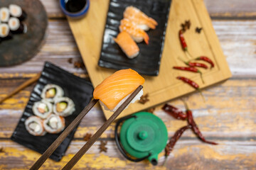 Wooden chopsticks holding a Japanese Norwegian salmon nigiri and sushi plates in the background