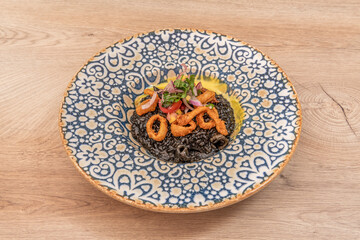 Squid risotto nero stewed with red onion and battered squid rings on a porcelain plate decorated in blue and white