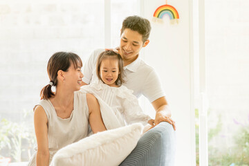 HERMOSA FAMILIA ASIÁTICA MUY SONRIENTES SENTADOS EN EL SOFÁ DE SU HOGAR CON UN ARCOIRIS EN LA...