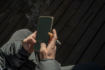 Man hands typing a message on the phone smoking a cigar outdoors