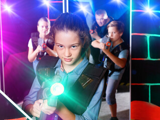 Fototapeta na wymiar Portrait of positive smiling teenager girl with laser gun having fun with her family on lasertag arena