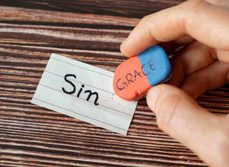 Sin and grace handwritten words on paper and rubber eraser in woman's hand on wooden table...