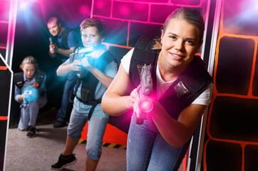 Emotional girl with laser pistol playing laser tag with friends on dark labyrinth