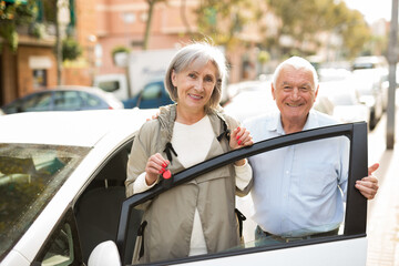 Mature woman and man standing beside car, woman holding keys in hand.