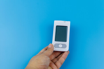 Digital glucometer in female hand over a pastel blue background. Diabetes concept