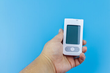 Digital glucometer in female hand over a pastel blue background. Diabetes concept