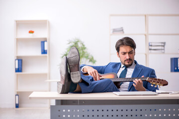 Young male employee playing guitar at workplace