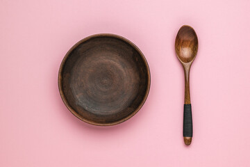 A clay plate and a stylish wooden spoon on a pink background. Vintage tableware.