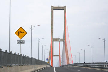 Scene of the famous Suramadu Bridge and its red suspension steel cables with lamp post on road and cloudy sky background