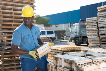 African-american man carrying hollow concrete blocks in outdoor construction material warehouse.