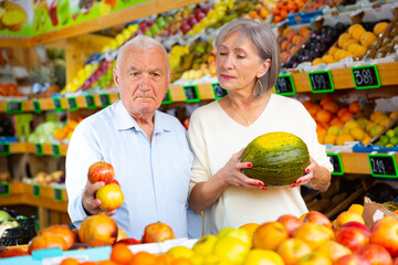 Fototapeta premium European old man and woman choosing fresh fruits in greengrocer.