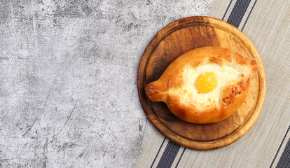 Caucasian flat bread - Adjarian khachapuri with cheese and egg on a round wooden cutting board on a dark grey background. Top view, flat lay.