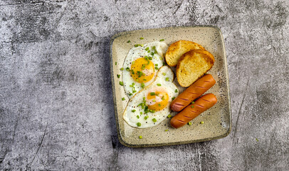 Easy breakfast - fried eggs and sausages with toast on a square  plate on a dark background. Top view, flat lay
