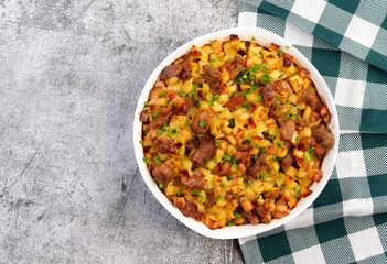 Oven baked meat with potatoes and herbs in a white baking dish on a dark grey background. Top view, flat lay