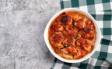 Chicken in tomato sauce in a white baking dish on a dark grey background. Top view, flat lay