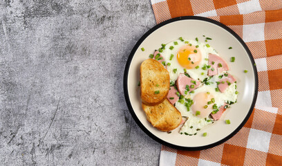 Easy breakfast - fried eggs and sausages with toast on a round plate on a dark gray background. Top view, flat lay  .