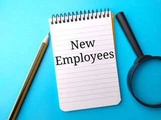 Pencil,magnifying glass and notebook with text New Employess on a blue background.