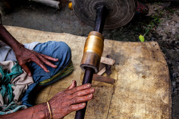 Close up of man's hand extracting silk strands from cocoons using a wooden spindle.