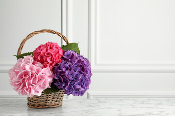 Bouquet with beautiful hortensia flowers in wicker basket on white marble table. Space for text