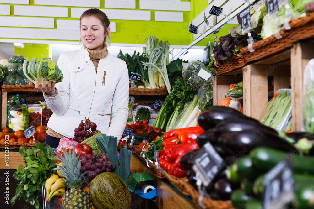 Wall mural Young attractive woman choosing fresh vegetables in greengrocery