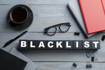 Black cubes with word Blacklist, cup of coffee and office stationery on grey wooden table, flat lay