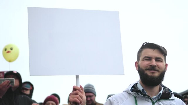 Young adult bearded guy holding blank copyspace chromakey advertise banner on protest. Empty ads board card with motion tracking points. Clear advert sign panel poster for mockup advertising text.