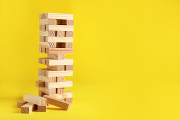 Jenga tower made of wooden blocks on yellow background, space for text