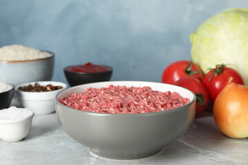 Minced meat in bowl and other ingredients for stuffed cabbage rolls on grey table