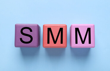 Colorful cubes with abbreviation SMM (Social media marketing) on light blue background, flat lay